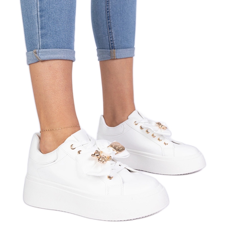Zapatillas blancas decoradas con un arco y un oso de peluche dorado blanco